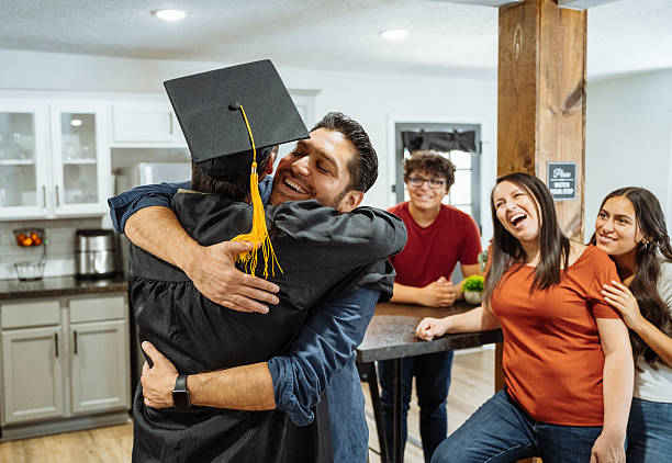 istock Graduation celebration at home - father hugging son in graduation gown 2232059444