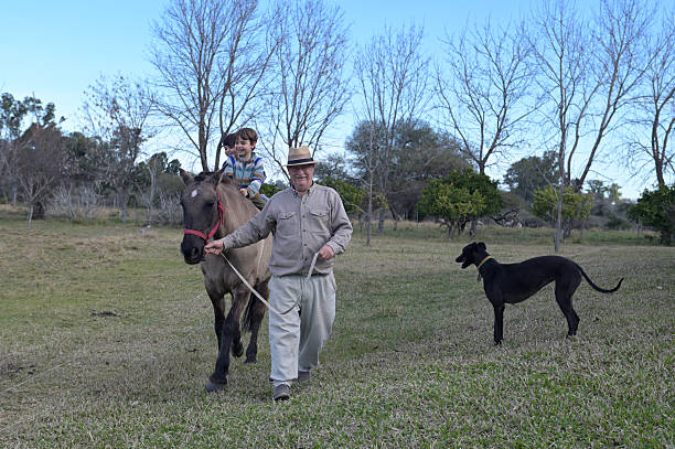 grandfather taking his nephews for a ride on horseback in the countryside with his dog