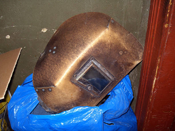 old welding mask with tinted glass lying on blue plastic bag. Mask is worn and covered with film, Background of peeling wall, industrial and abandoned atmosphere