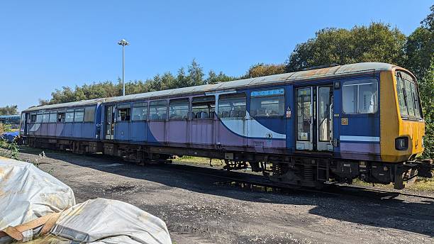 Abandoned locomotive engine, train car carriages, rusting railroad tracks. Derelict public transport, run down railway line. Sad commuter railcar vandalised, broken windows, dirty, falling apart. Old fashioned era train carriage commuting railway cars, deserted and dilapidated. Sunny summers day, blue clear sky. Shabby rail depot yard. Disused transportation on failing british rail. Deteriorating, wrecked non high speed train for travelling.