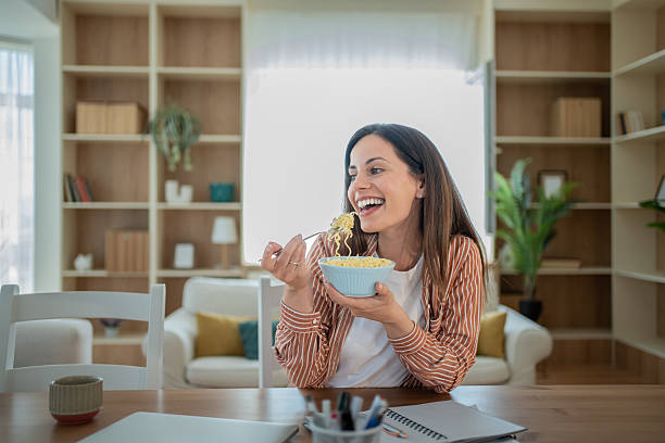 istock Happy freelancer woman eating noodles while working from home 2232069743