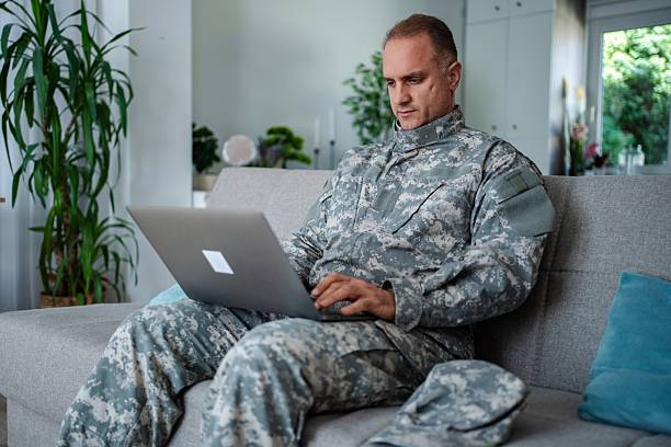 istock Soldier in camouflage uniform using laptop on sofa at home 2232070399