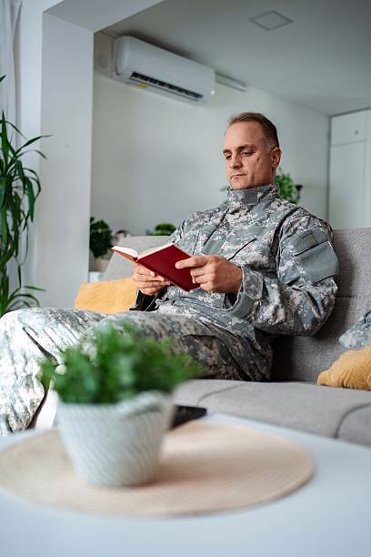 istock Soldier relaxing on sofa reading a book at home 2232070403