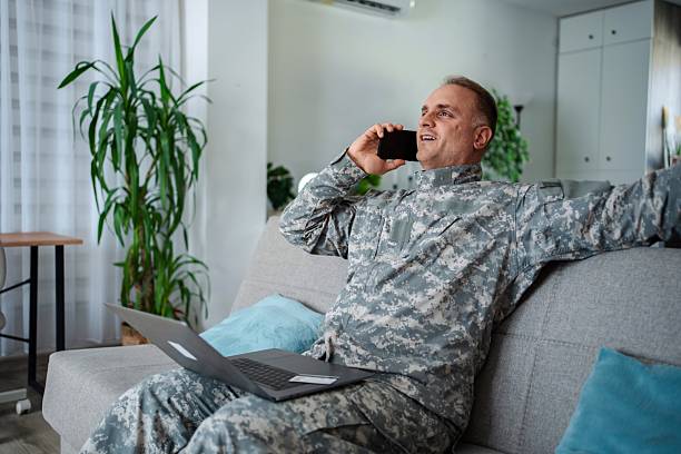 istock Happy Soldier Relaxing on Sofa, Talking on Phone and Using Laptop 2232070467