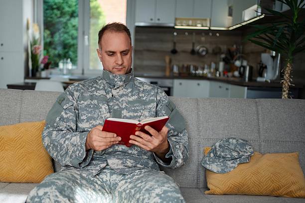 istock Soldier reading a book sitting on the sofa at home 2232070509