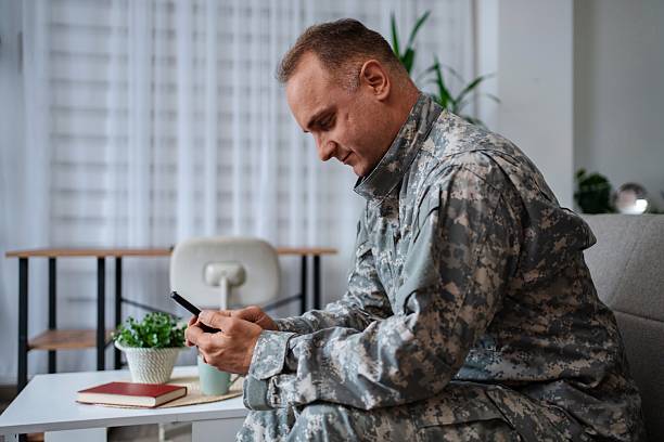 istock Soldier in camouflage uniform using smartphone at home 2232070572
