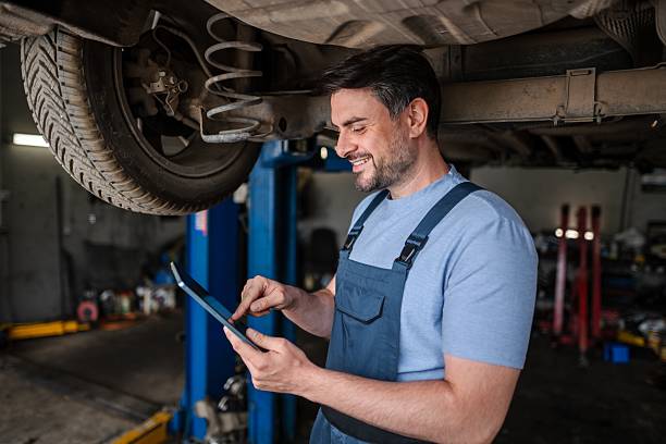 istock Car mechanic using a digital tablet while working under a lifted car in a repair shop 2232071126