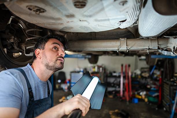 istock Mechanic inspecting car chassis with a lamp in a garage 2232071299