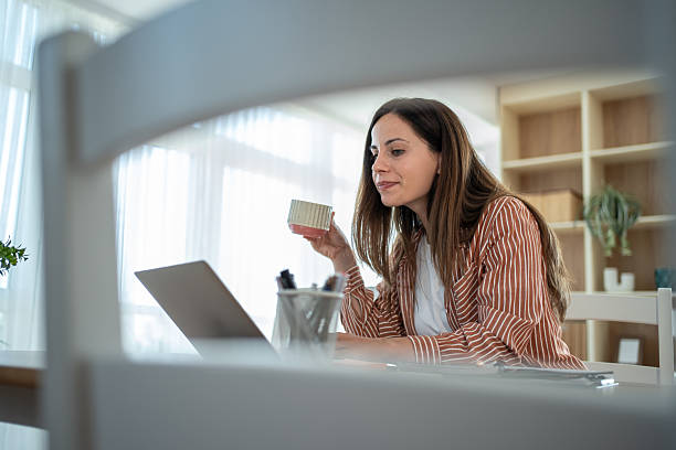 istock Young woman working from home drinking tea and using laptop 2232072062