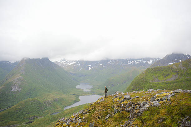 Distant view of young woman on mountain ridge above archipelago, Svolvaer, Lofoten Islands
