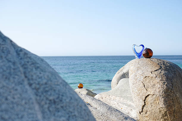 Stable balanced cairn of polished sea glass stones on a wooden log on the seashore.