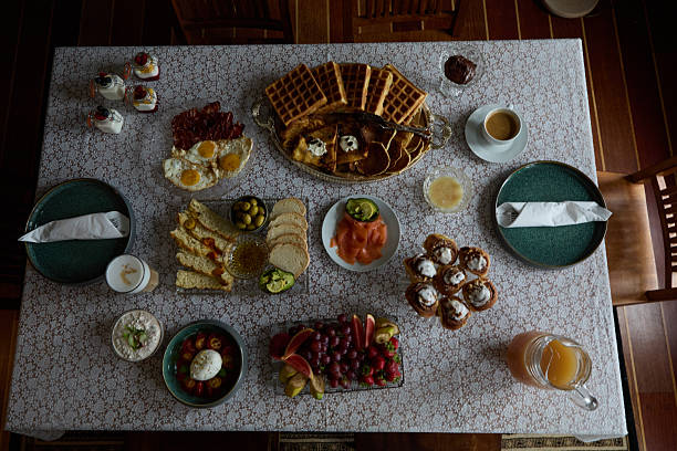 An inviting breakfast table featuring various delicious foods including fruits, waffles, pastries, and beverages, presented on a beautifully decorated tablecloth, creating a warm and delightful dining experience.