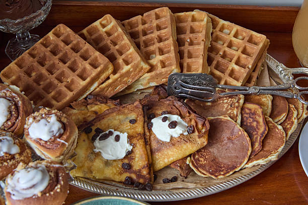 A delicious spread featuring waffles, sweet crepes, fluffy pancakes, and icing-topped cinnamon rolls served on a decorative platter.