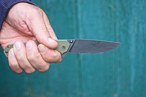 istock man hand holding black army folding knife against green wall 2232081541