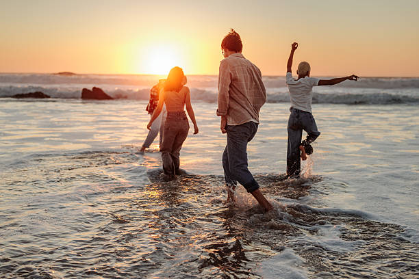 istock Friends walking in ocean waves at sunset enjoying summer vacation 2232084639