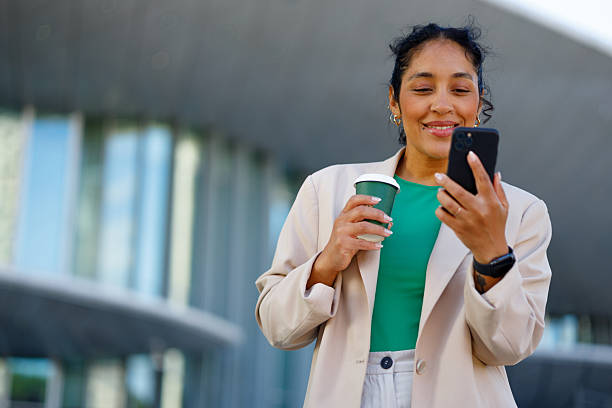istock Businesswoman enjoys a coffee while checking her smartphone in front of a modern office building 2232087699