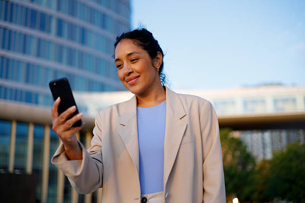 istock Businesswoman smiling while using her smartphone in front of a sleek modern office building, enjoying the vibrant city atmosphere 2232090157