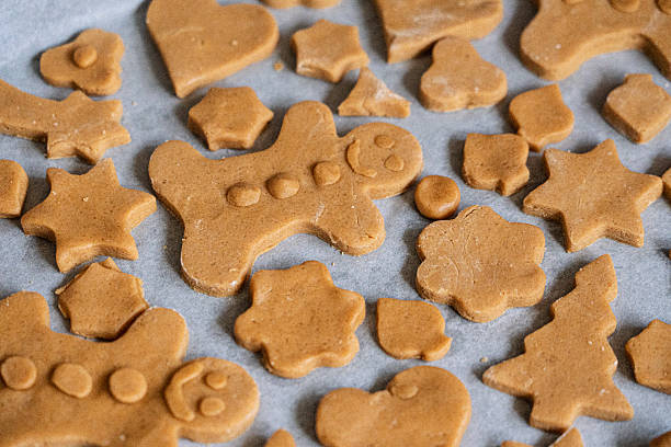 Smiling gingerbread man cookie surrounded by gingerbread cookies in diverse shapes, heart, star, flower, shamrock, all arranged on baking paper. Christmas background.