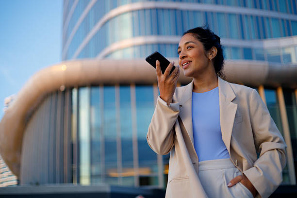 istock Young businesswoman using smartphone voice assistant while standing in front of modern office building 2232091511
