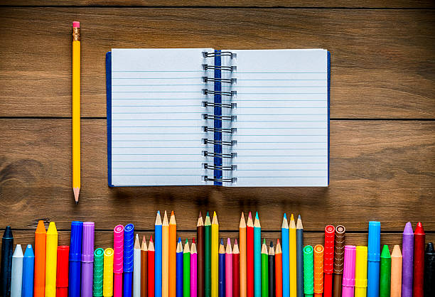 istock Top view of wood table with assorted multi colored pencils and markers. Note book into the frame. 2232105445
