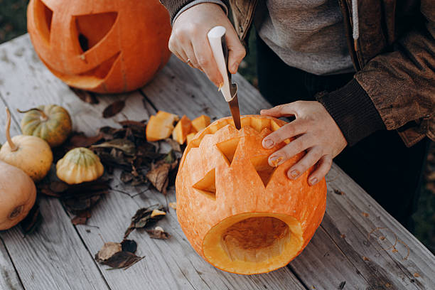 istock Making a jack o lantern. Hands carving halloween pumpkin on rustic wooden table in autumn garden, hands close up. Fall harvest. Cutting pumpkin. Halloween preparation 2232110213