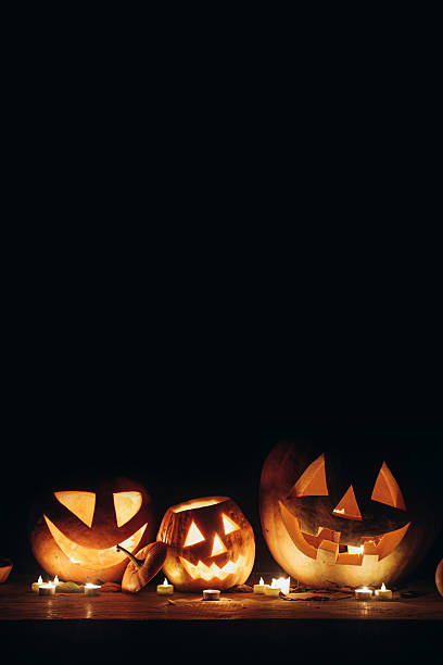 Spooky glowing Jack o lantern and candle light on rustic wooden table in dark autumn night. Happy Halloween! Scary atmospheric carved pumpkins in evening. Boo! Trick or treat. Copy space