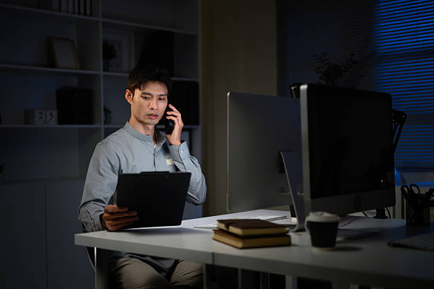 istock Asian businessman working late in office, talking on phone while checking documents 2232112957