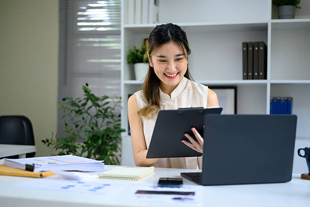 istock Smiling businesswoman reviewing documents while working with laptop in modern office 2232113063