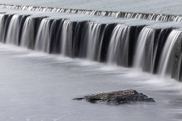 istock High resolution long exposure photography of artificial waterfall with soft blurred water streams falling over stone edge and rock detail in foreground, river landscape captured in natural light 2232113477