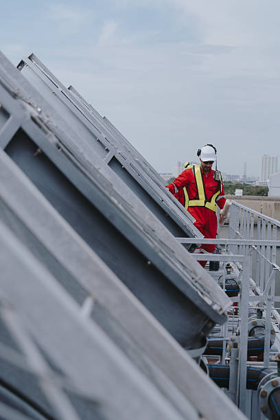 Industrial engineers working as a team, maintaining pipes, valves, air conditioning, refrigeration, HVAC systems at construction site. Male technicians in red safety uniforms checking pipe valves.