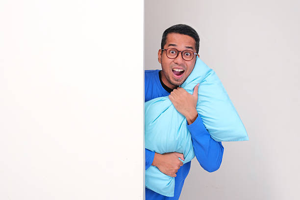 istock Adult Asian man peeking behind wall while hugging a pillow with excited expression 2232123343