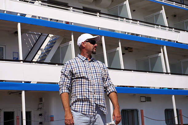 Mature man wearing sunglasses and white cap standing near river cruise ship on sunny day