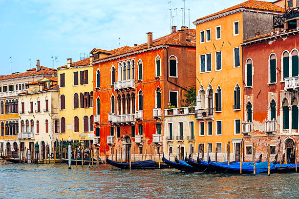 Scenic view of vibrant Venetian architecture lining a peaceful canal, showcasing traditional gondolas docked along the wooden piers, capturing the essence of Venice, Italy’s rich cultural and architectural heritage.