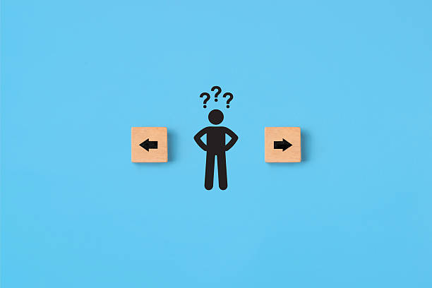 istock Decision making and choosing the right path. Confusion about deciding which direction to go. Stickman with question marks standing in between the wooden cubes with arrow symbols 2232136075