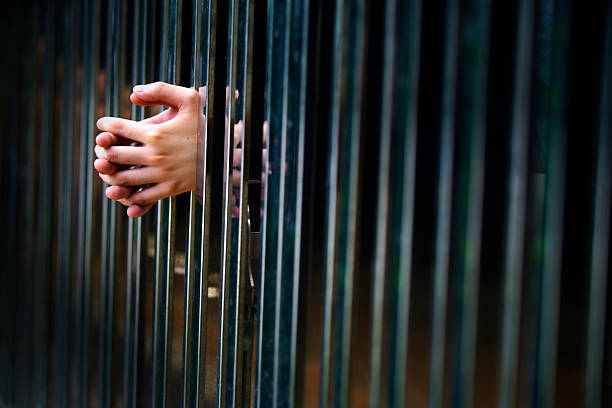 A close-up image of hands gripping metal bars, evoking themes of confinement and emotional struggle. The interplay of light and darkness adds depth.