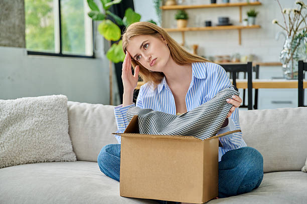 istock Sad young woman unpacking online purchase, looking at new clothes 2232143377