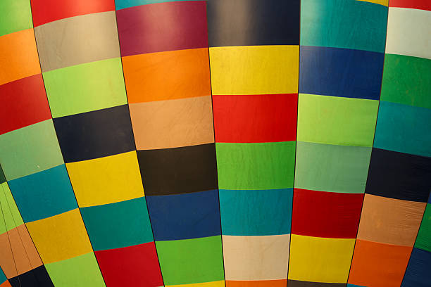 A vibrant close-up of a hot air balloon’s fabric showcases a striking patchwork of bold, colorful squares. The geometric pattern and vivid hues capture the spirit of adventure and the festive atmosphere of ballooning events.