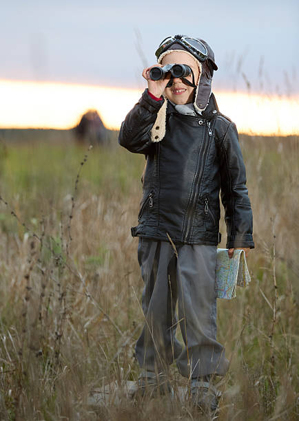 The nice boy preschool age dressed in a retro aviator costume. The boy is standing in the meadow among the grass. Shooting outdoors at autumn evening at sunset