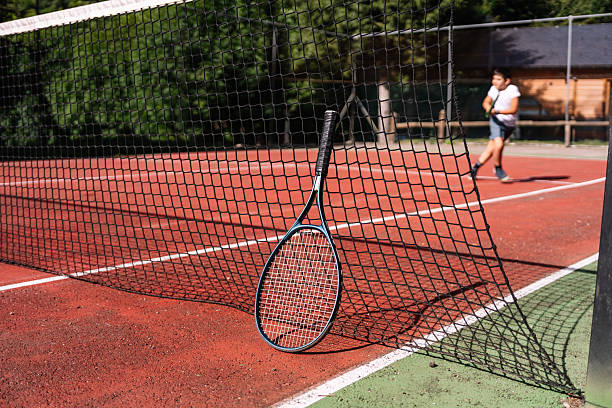 istock Tennis racket leaning on net with child practicing in background on sunny day 2232150990