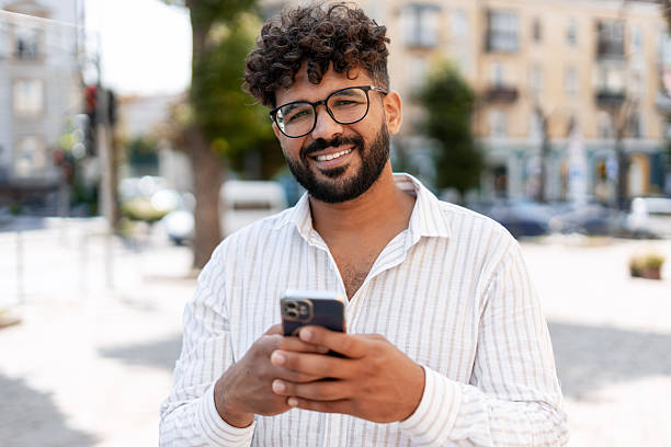 istock Young man using mobile phone and smiling in city street 2232152667
