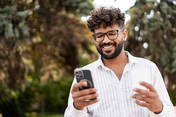 istock Young Indian Man Enjoying a Coffee and Browsing his Smartphone in a Park 2232153523