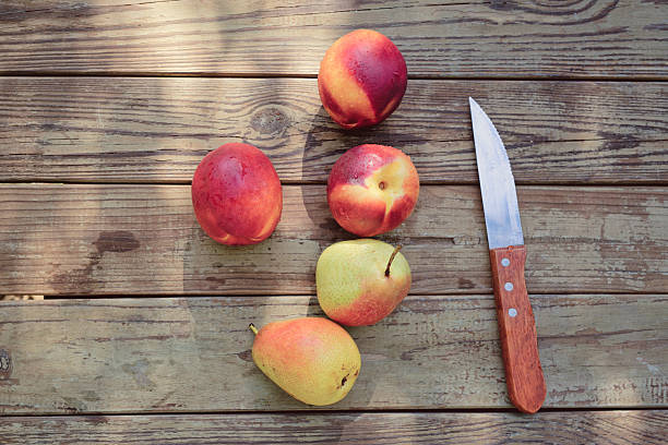 A collection of ripe nectarines and pears sits on a rustic wooden table, accompanied by a kitchen knife, showcasing a vibrant and refreshing summer fruit display. Copy space for text - healthy living, summer fruit