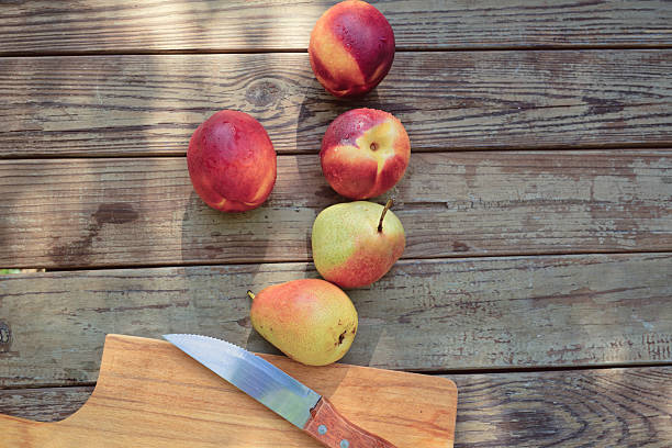 A vibrant arrangement of nectarines and pears sits on a wooden table under dappled September sunlight. The fruits are fresh, showcasing their natural colors, ideal for a summer snack. Copy space for text - healthy lifestyle, food