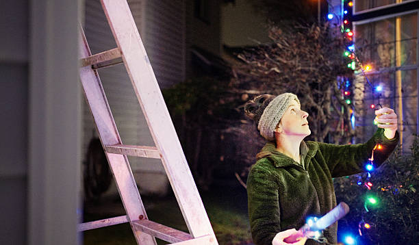 istock Woman decorating outside house with Christmas lights on a cold night 2232155406