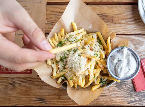 Hand reaching for gourmet fries topped with herbs and cheese at a rustic dining setting in a casual eatery
