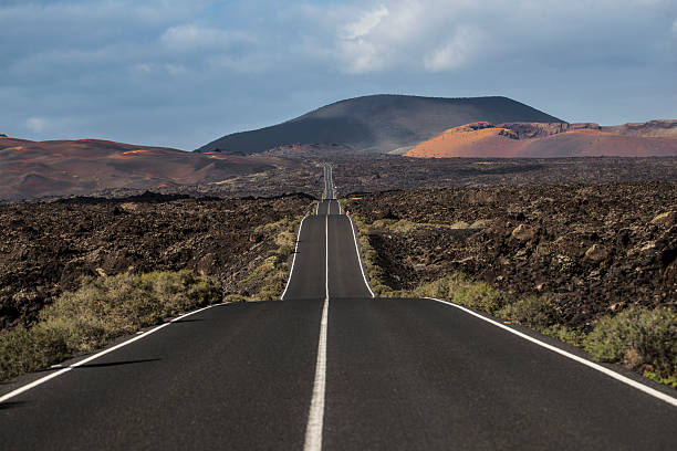 istock Long empty road crossing volcanic landscape in lanzarote 2232172735