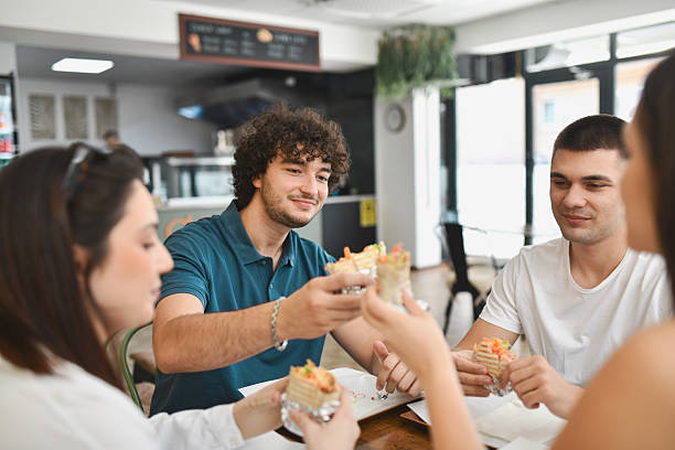 istock Cheerful Friends Smiling Brightly While Clinking Generous Wrap Sandwiches Before Taking Bite 2232173672