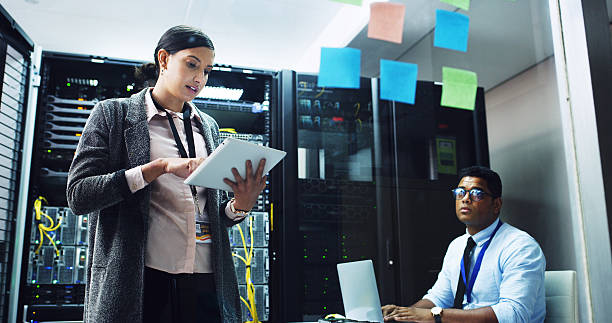 istock Woman, tablet and talk with man in server room, programming or glass wall for IT solution at company. People, planning and talk with tech, application or information technology for system maintenance 2232174339
