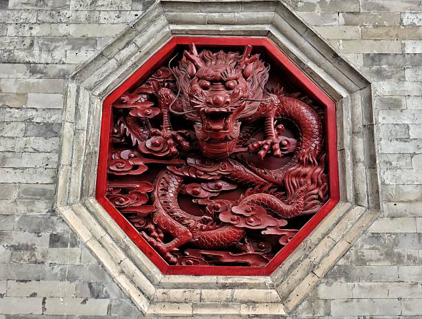 Close-up of a powerful, meticulously detailed red lacquered dragon carving set into a weathered stone wall. The vibrant crimson finish contrasts dramatically with the rough, textured grey masonry, creating a striking visual of myth and history. This image symbolizes strength, protection, and Eastern tradition, perfect for concepts on mythology, heritage, power, and cultural design.