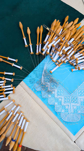 Intricate lace creation process featuring organized wooden bobbins surrounded by delicate threads arranged on fabric using traditional handcrafting techniques.